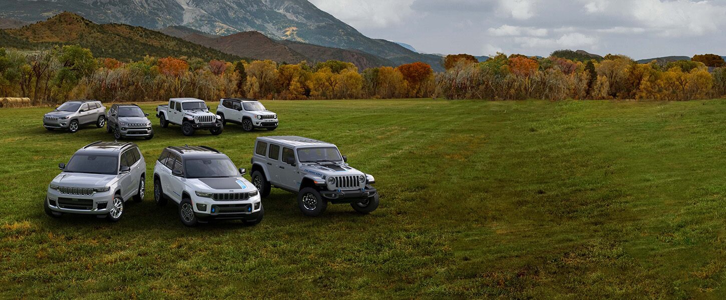 Una formación de siete vehículos Jeep 2022 estacionados en una planicie cubierta de césped, con un bosque otoñal y montañas que se elevan a la distancia.