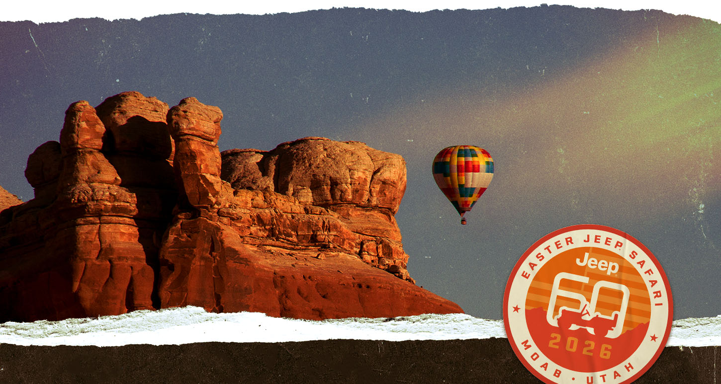 Una formación rocosa gigante en el desierto, con el suelo nevado y un globo aerostático a la distancia. Easter Jeep Safari. Jeep 60 2026. Moab, Utah.