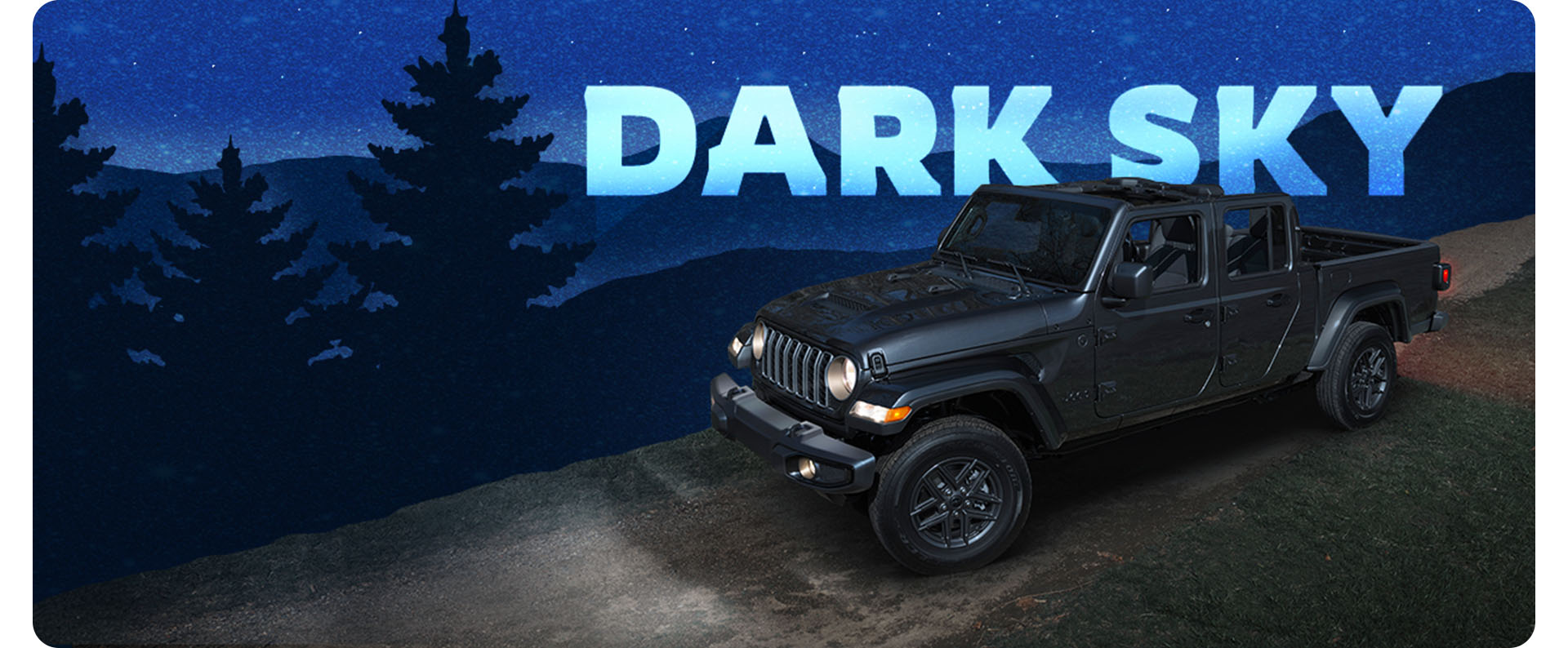 Ángulo delantero del lado del pasajero de un Jeep Gladiator Sport S 2025 en gris oscuro con el paquete Dark Sky en un camino de tierra, con los faros delanteros encendidos y el techo extraído. Paquete Dark Sky.