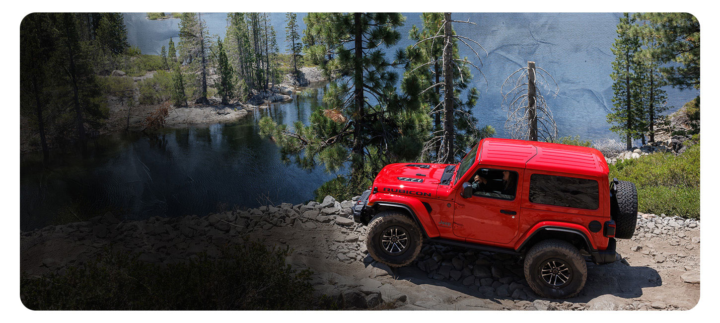 Un Jeep Wrangler Rubicon X 2025 rojo estacionado en un peñasco rocoso con vista a Lake Tahoe y a un bosque tupido.