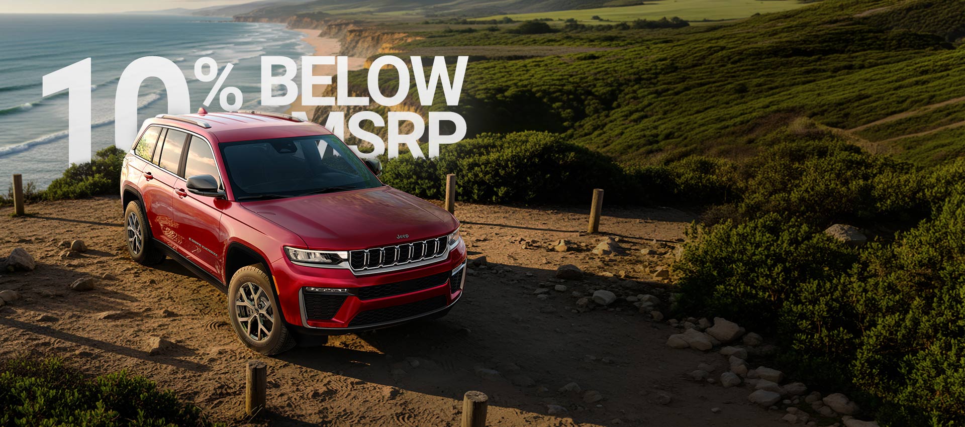 A red 2026 Jeep Grand Cherokee Limited parked on a beach near the shoreline. 520 + Miles.