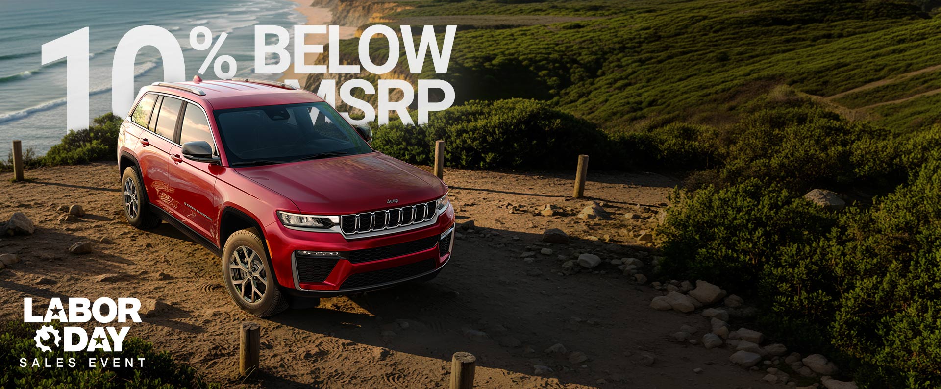 Un Jeep Grand Cherokee Limited 2026 rojo estacionado en una playa cerca de la orilla. 520 + millas. Evento de ventas por el Día del Trabajo.